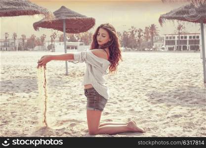 Teen girl on the beach playing with sand near thatch umbrellas filtered image