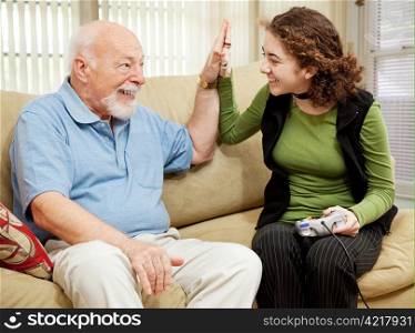 Teen girl playing video games, getting a high five from her grandfather.
