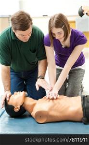 Teen girl practicing CPR on a mannequin, with her teacher&rsquo;s help.