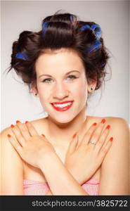 Teen girl preparing to party. Portrait of young woman with hair curlers pin up makeup red lips and nails studio shot on gray. Hairstyle and manicure.