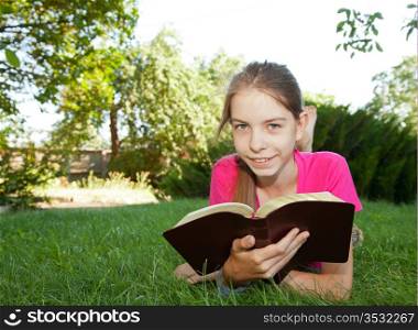 Teen girl reading the Bible outdoors lying on the grass