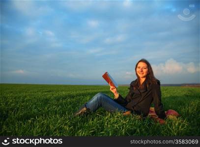 Teen girl reading the Bible sitting outdoors at sunset time