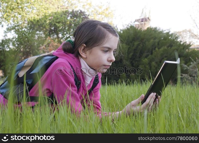 Teen girl reads electronic book laying on the grass