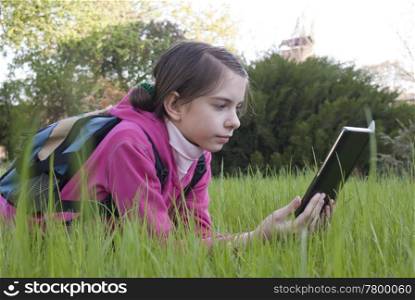 Teen girl reads electronic book laying on the grass