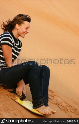 teen girl riding on the sand dunes sandboard in the Arabian desert