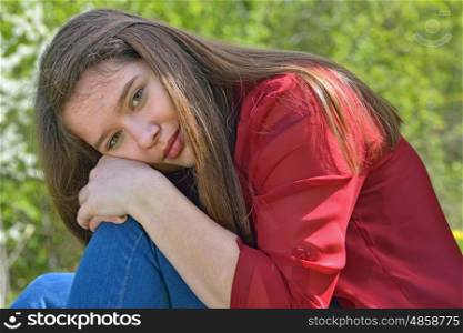 Teen girl sits hugging her knees outdoors