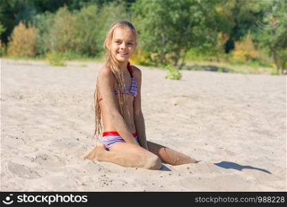 Teen girl sits on a river sandy river beach