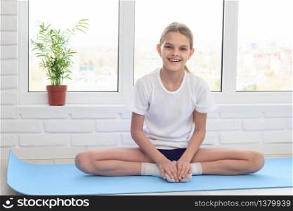 Teen girl sitting on a sports mat before training at home