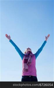 Teen girl staying with raised hands against blue sky