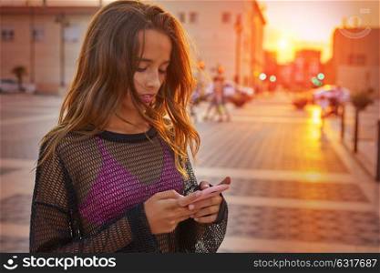 Teen girl texting chat on smartphone at sunset in the city