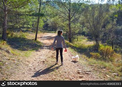 Teen girl walking with a white maltichon dog in forest track
