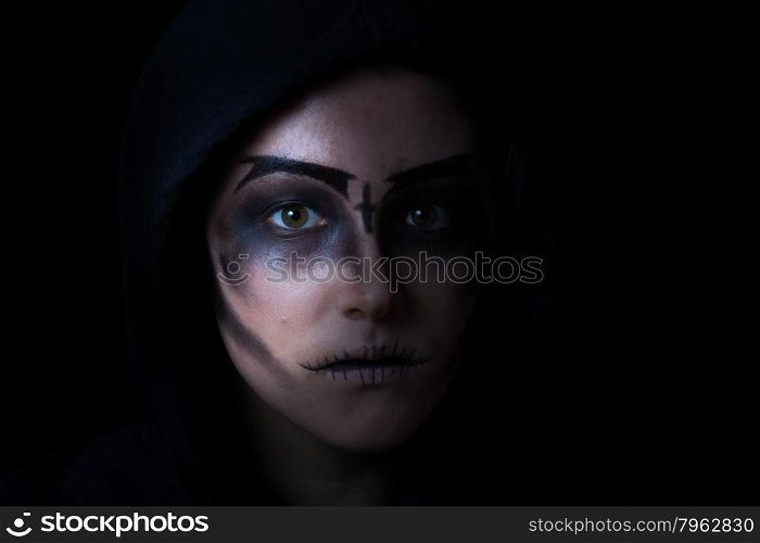 Teen girl wearing hoodie with scary face makeup on black background.