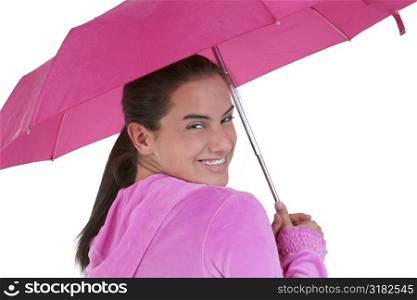 Teen girl with big smile and braces wearing pink under a pink umbrella.