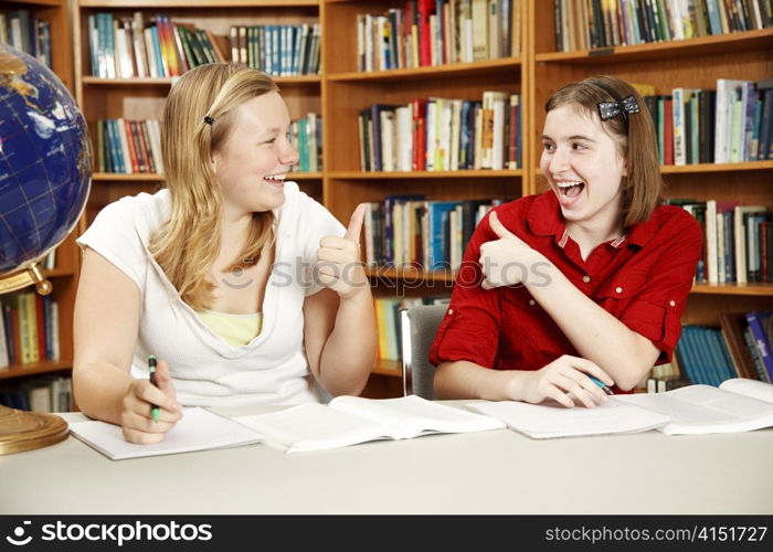 Teen girls doing their homework in the school library and giving each other the thumbs-up sign.