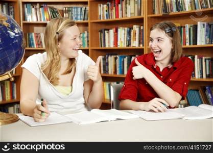 Teen girls doing their homework in the school library and giving each other the thumbs-up sign.