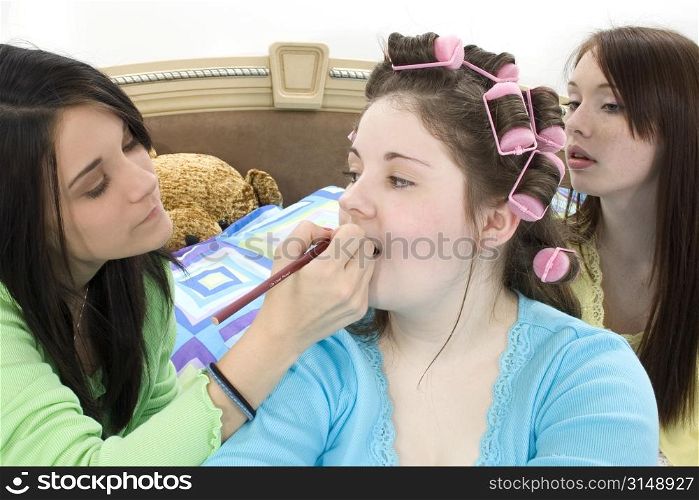 Teen girls in pajamas giving friend a make-over at sleepover.