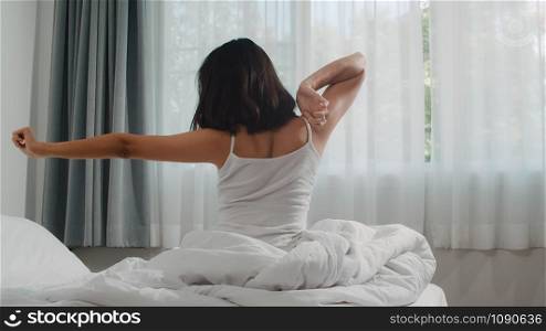 Teen hispanic woman wakes up at home. Young Asian girl stretching after awake sleep all night starting a new day with energy and vitality felt very refreshed on bed near window in bedroom at morning.