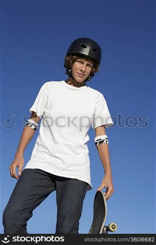 Teenage boy (16-17) holding skateboard outdoors, portrait