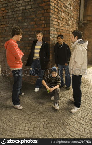 Teenage boy crouching with his friends standing around him