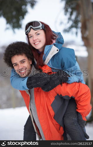 Teenage Boy Giving Girl Piggyback In Snowy Landscape