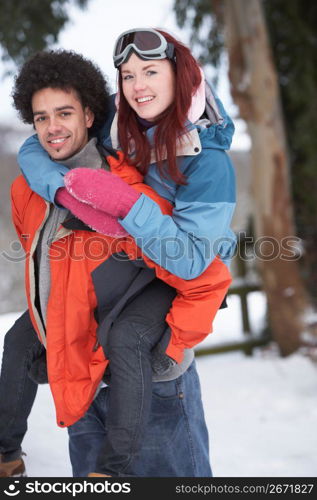 Teenage Boy Giving Girl Piggyback In Snowy Landscape