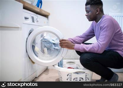 Teenage Boy Helping With Domestic Chores At Home Emptying Washing Machine