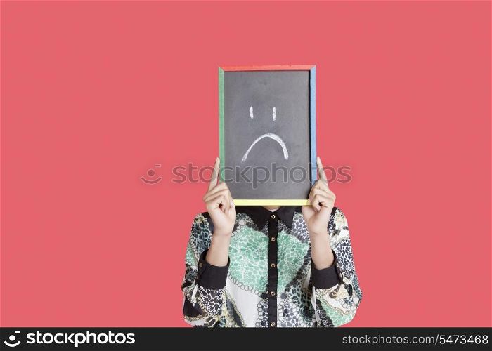Teenage boy holding slate with sad smiley on it over red background