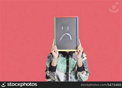 Teenage boy holding slate with sad smiley on it over red background