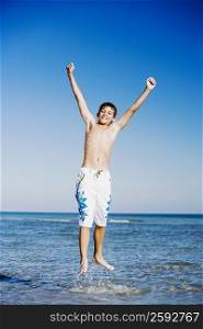 Teenage boy jumping in water with his arms raised