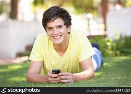 Teenage Boy Laying In Park Using Mobile Phone
