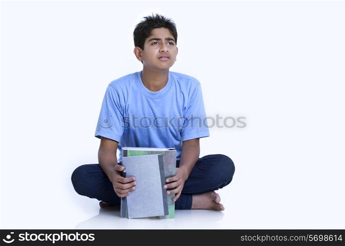Teenage boy looking away while holding books against white background