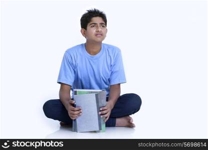 Teenage boy looking away while holding books against white background