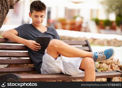 Teenage Boy On Park Bench Using Digital Tablet