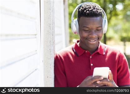 Teenage Boy Outdoors Streaming Music From Mobile Phone To Wireless Headphones