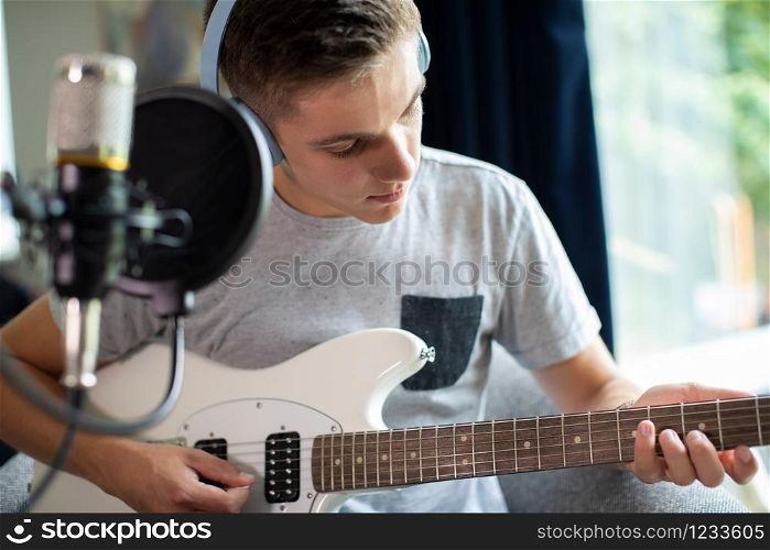 Teenage Boy Playing Guitar And Recording Music At Home