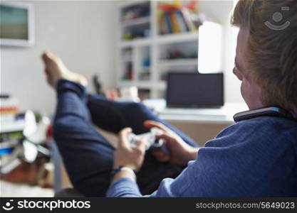 Teenage Boy Playing Video Game And Talking On Mobile Phone