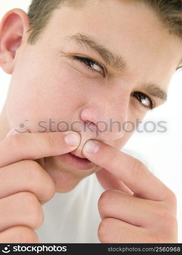 Teenage boy popping zit on face