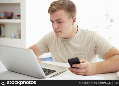 Teenage Boy Sending Text Message Whilst Studying On Laptop