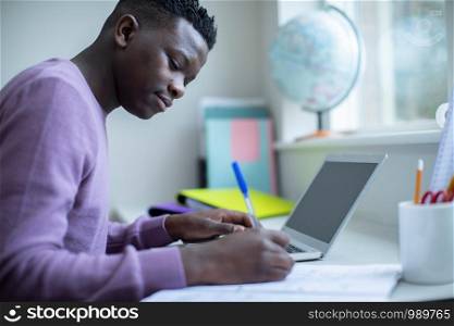 Teenage Boy Sitting At Desk Doing Homework Assignment On Laptop