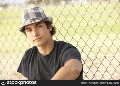 Teenage Boy Sitting In Playground Wearing Hat
