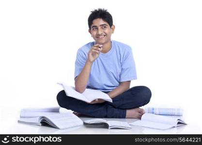 Teenage boy sitting on floor thinking while studying against white background