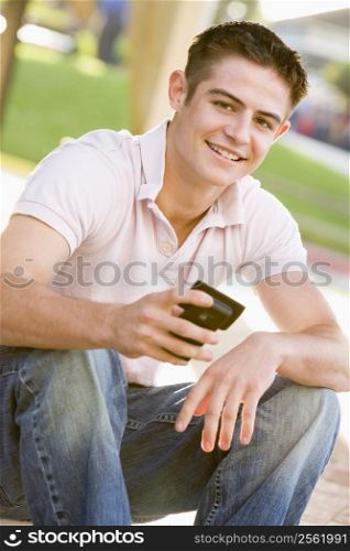 Teenage Boy Sitting Outdoors Using Mobile Phone