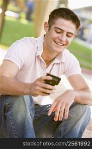 Teenage Boy Sitting Outdoors Using Mobile Phone