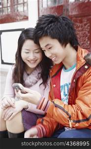Teenage boy sitting together with a young woman holding a mobile phone