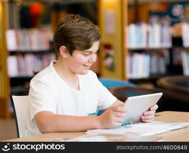Teenage boy sitting with tablet in library. Teenage boy with tablet in library