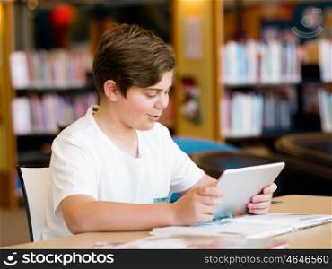 Teenage boy sitting with tablet in library. Teenage boy with tablet in library