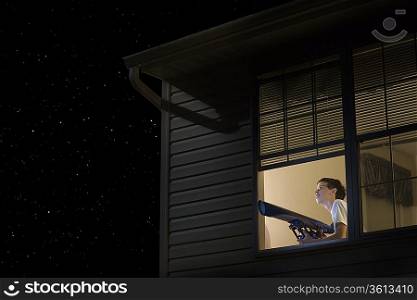 Teenage boy stands with telescope at open window looking at night sky