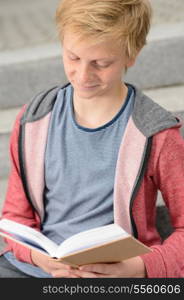 Teenage boy studying reading book while sitting on school steps