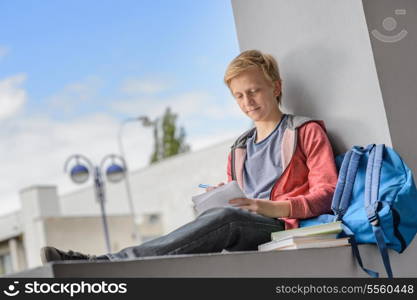 Teenage boy studying while sitting on wall at university campus