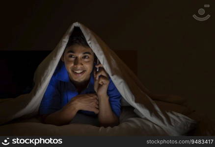 Teenage boy talking on his mobile phone in a dark room.